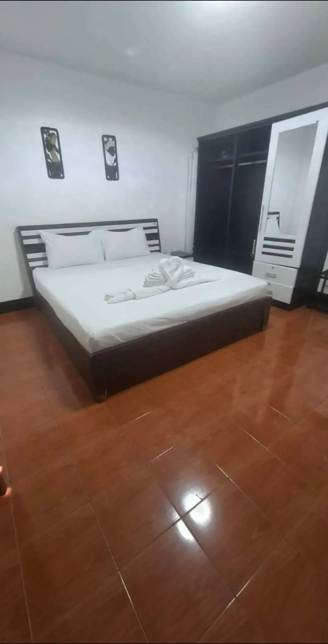 Double bed beside a tall dark wardrobe on polished tile flooring